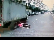 Китаянка, упавшая под колеса грузовика, чудом осталась невредима (видео) 