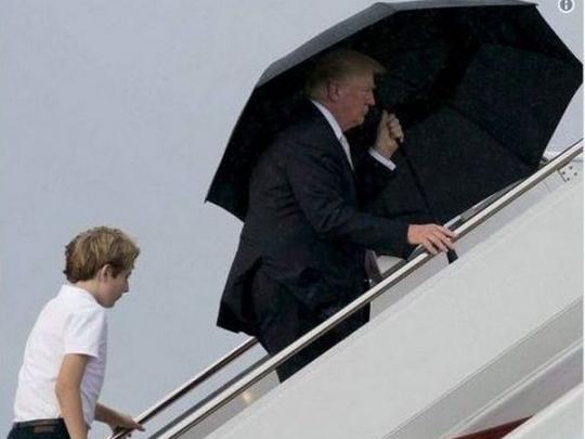 Трамп поднимается по трапу с зонтом, сзади&nbsp;— его сын