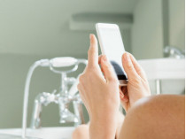 Девушка держит в руках телефон, принимая ванну