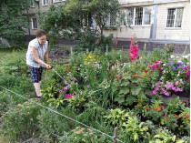 женщина поливает цветы возле дома