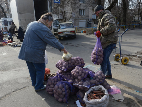 Женщина покупает картофель на уличной распродаже